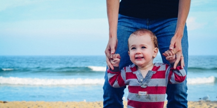 Mand holder lille barn i hånden ved stranden
